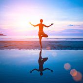 stock photo of sunset  - Young woman practicing yoga on the beach at sunset with reflection in water - JPG 