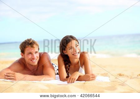 Picture or Photo of Couple on beach looking happy during summer travel vacation holidays. Multiracial young couple lying in sand on beach on looking to side. Asian woman, Caucasian man.