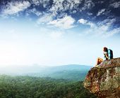 foto of woman  - Young woman with backpack sitting on cliff and looking to a sky - JPG 