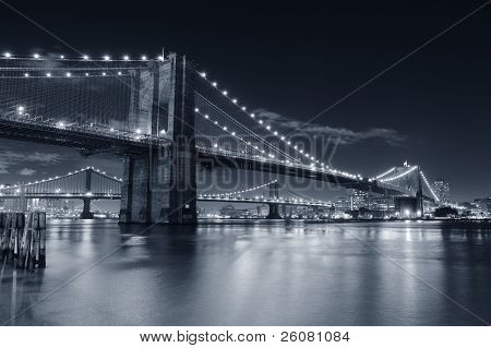 Picture or Photo of Brooklyn Bridge over East River at night in black and white in New York City Manhattan with lights and reflections.