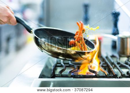 Picture or Photo of Chef in restaurant kitchen at stove with pan, doing flambe on food