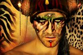 foto of animals  - Fashion stylized concept portrait of a young man with tribal face painting and animal elements in front of a animal print background - JPG 