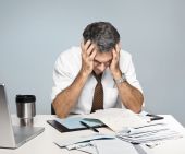 stock photo of worry  - Man at desk in shirt and tie holding his head and worrying about money and the economy - JPG 