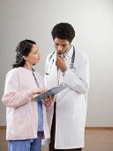 image of medical doctors  - Serious doctor in lab coat listening to nurse explain medical chart - JPG 