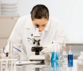 stock photo of science  - Curious research scientist in lab coat and rubber gloves looking at specimen under microscope in laboratory - JPG 
