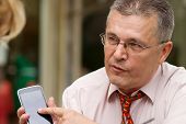 stock photo of respect  - Respectable senior businessman showing something to his colleague on his trendy smart phone - JPG 
