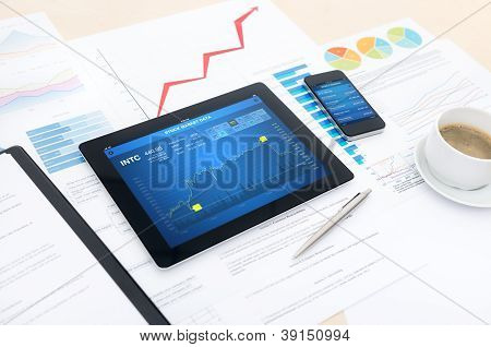 Picture or Photo of Modern business workplace with stock market data on  apple ipad and mobile banking apps on apple iphone and many charts and graphs on a desktop.