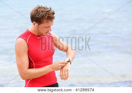 Picture or Photo of Athlete runner looking at heart rate monitor watch. Man running on beach taking a break in compression t-shirt top.