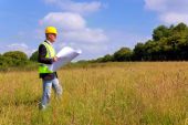 stock photo of survey  - Architect wearing site safety gear and holding plans surveying a new building plot - JPG 