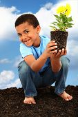 stock photo of earth  - Adorable  Black Boy Child Planting Flowers for Earth Day Barefoot in Soil Holding Flower - JPG 