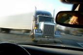stock photo of truck  - Close call imminent crash accident with a tractor trailer truck viewed from inside a passenger car with scared driver face in rear view mirror - JPG 