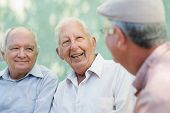 stock photo of group  - Active retirement group of three old male friends talking and laughing on bench in public park - JPG 