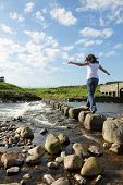 stock photo of step  - Young girl runs across stepping stones  to cross a stream - JPG 