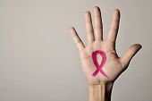 closeup of the palm of a young caucasian man with a pink ribbon for the breast cancer awareness pain