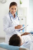 stock photo of medical doctors  - Smiling female doctor looking a the patient lying on the couch - JPG 