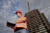 foto of construction worker  - Construction supervisor in safety helmet and reflex vest with notebook in front of construction site - JPG 