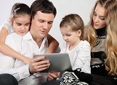 stock photo of home  - Happy family of mother father and daughters sitting on a sofa at home having fun using a tablet computer - JPG 