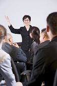 picture of group  - Hispanic woman standing in front speaking to group of business people - JPG 