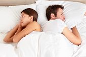 pic of man  - Upset young couple having marital problems or a disagreement lying side by side in bed facing in opposite directions ignoring one another - JPG 