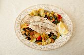 Fish fillet baked with vegetables, Italian dish, on restaurant table shot from above