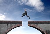 picture of gap  - Businessman jumping over the gap between two parts of a bridge - JPG 