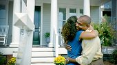 pic of home  - An African American couple stand outside a suburban home next to a For Sale sign and hug each other - JPG 