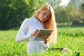 stock photo of outdoor  - Young  business woman sitting on grass and using electronic tablet outdoors - JPG 
