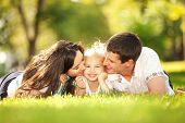 stock photo of nature  - Happy mother and father kissing their daughter in the park - JPG 