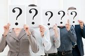 stock photo of group  - Group of business people hiding their faces behind a question mark sign at office - JPG 