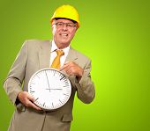 foto of watch  - Portrait Of A Senior Man Holding A Wall Watch On Green Background - JPG 