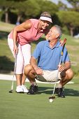 stock photo of golf  - Senior Couple Golfing On Golf Course Lining Up Putt On Green - JPG 