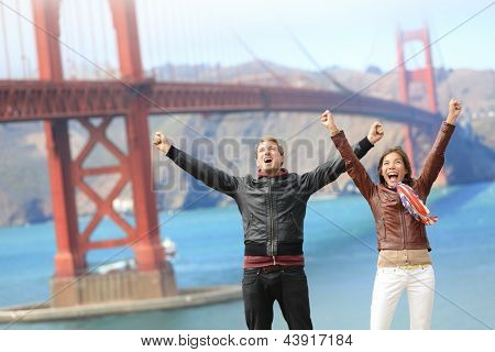 Picture or Photo of San Francisco happy people tourist couple at Golden Gate Bridge. Young attractive modern couple cheering happy, excited and joyful. California tourism concept with cheerful tourists.