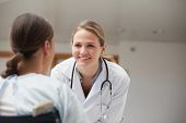stock photo of medical doctors  - Smiling doctor looking at a patient on a wheelchair in hospital hallway - JPG 