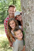 pic of family  - Smiling family standing behind a tree - JPG 